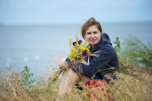 woman-sitting-grass-holding-flowers-wearing-black-hoodie-114825625